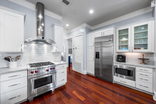 kitchen featuring white cabinets, dark hardwood / wood-style flooring, built in appliances, and wall chimney range hood