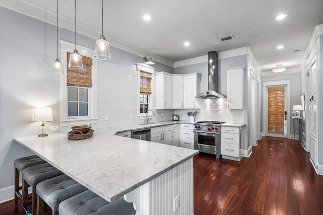 kitchen with kitchen peninsula, wall chimney exhaust hood, a breakfast bar, stainless steel appliances, and white cabinets