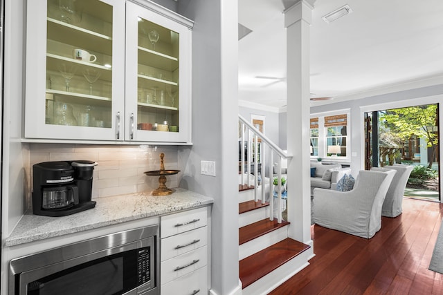 bar with decorative backsplash, dark hardwood / wood-style flooring, light stone counters, white cabinets, and stainless steel microwave