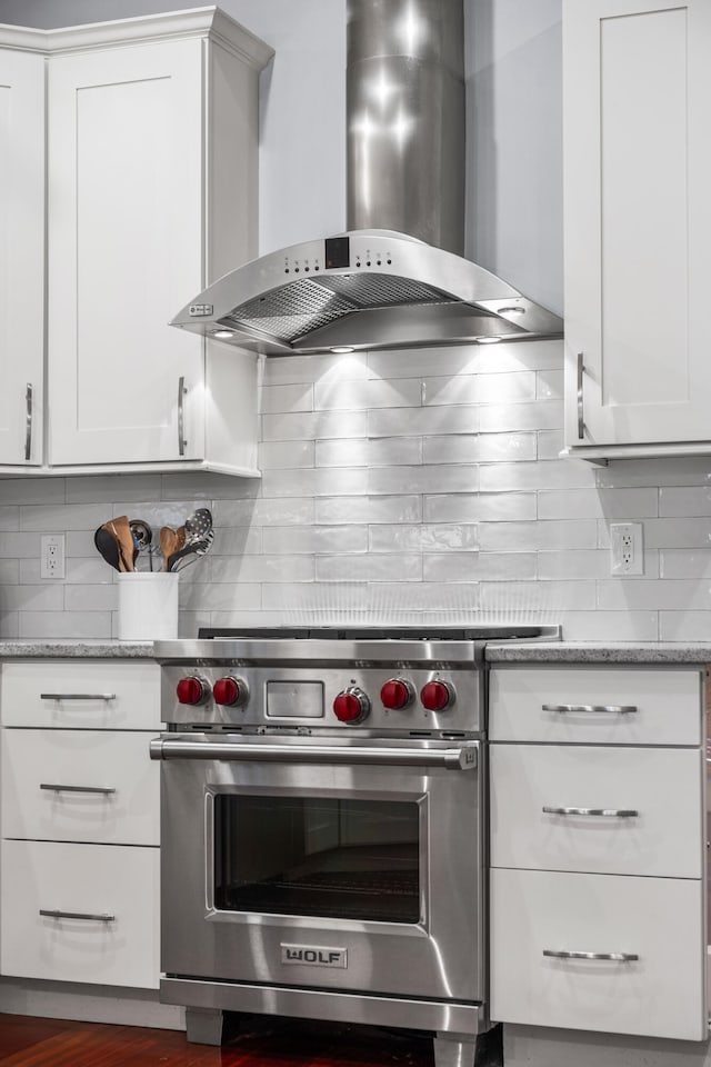 kitchen featuring wall chimney exhaust hood, light stone countertops, designer stove, tasteful backsplash, and white cabinetry