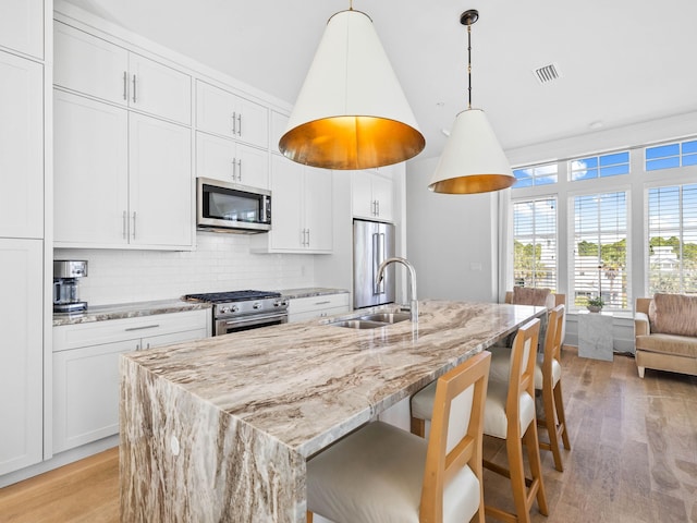 kitchen with sink, pendant lighting, high quality appliances, light hardwood / wood-style floors, and white cabinetry