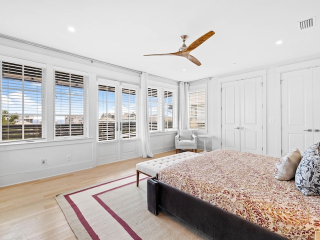 bedroom with light hardwood / wood-style flooring, ceiling fan, and multiple closets