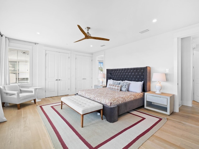 bedroom with ceiling fan, light wood-type flooring, and multiple closets