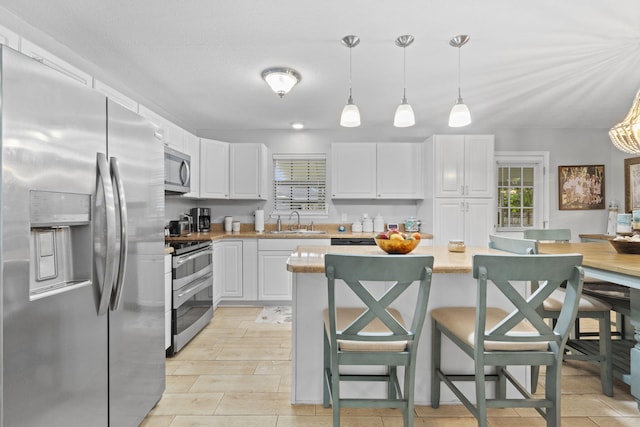 kitchen featuring pendant lighting, white cabinets, sink, appliances with stainless steel finishes, and a breakfast bar area