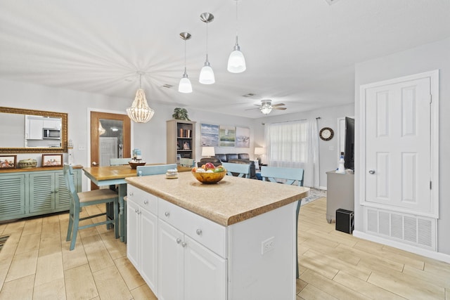 kitchen with ceiling fan with notable chandelier, white cabinets, light hardwood / wood-style floors, a kitchen island, and hanging light fixtures