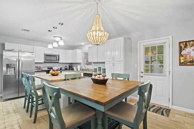 dining area with sink, a notable chandelier, and light wood-type flooring