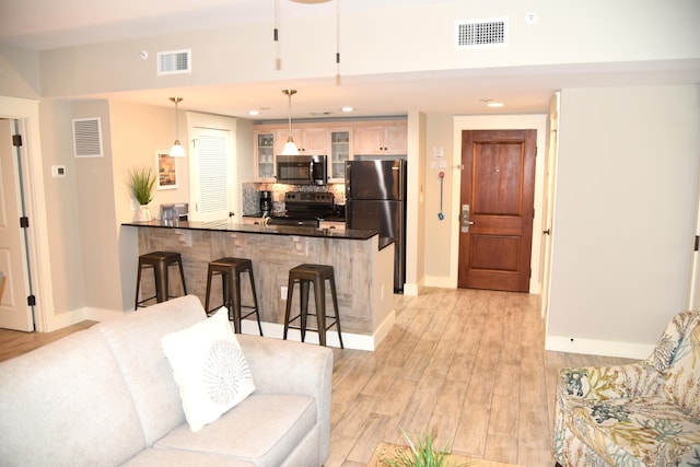 kitchen with kitchen peninsula, decorative light fixtures, a breakfast bar area, appliances with stainless steel finishes, and light wood-type flooring