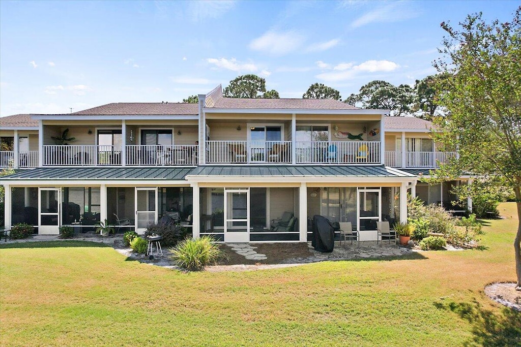 rear view of house with a balcony, a lawn, and a sunroom