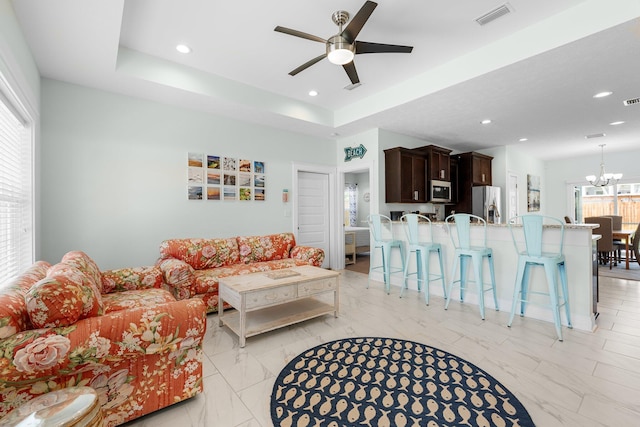 living room featuring a tray ceiling and ceiling fan with notable chandelier