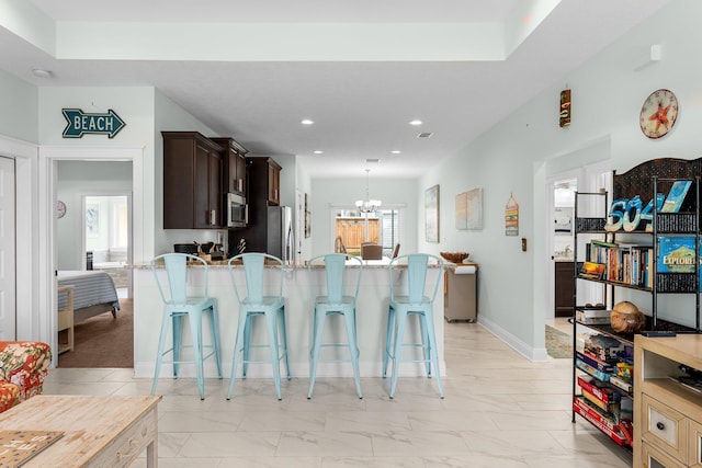 kitchen with a kitchen breakfast bar, a notable chandelier, pendant lighting, dark brown cabinets, and appliances with stainless steel finishes