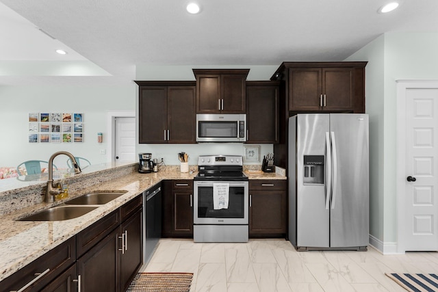 kitchen featuring dark brown cabinetry, sink, stainless steel appliances, light stone counters, and kitchen peninsula