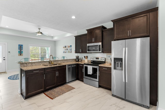 kitchen featuring sink, stainless steel appliances, light stone counters, kitchen peninsula, and dark brown cabinets