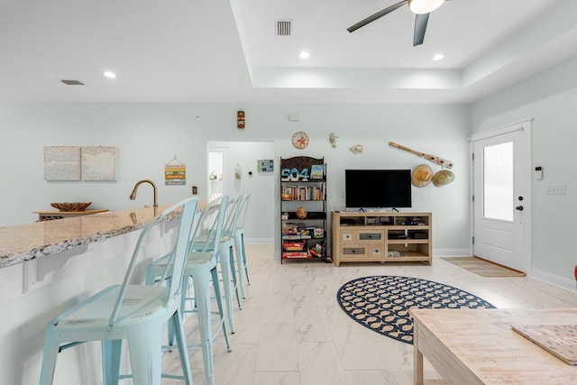 living room with ceiling fan, a raised ceiling, and sink