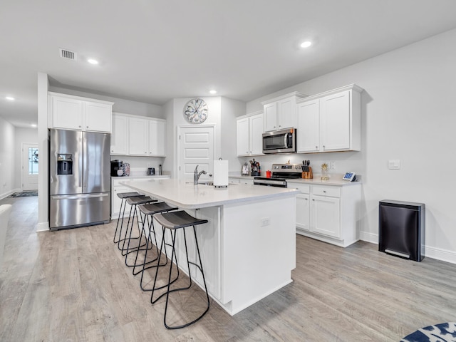 kitchen with light hardwood / wood-style flooring, stainless steel appliances, white cabinetry, and an island with sink