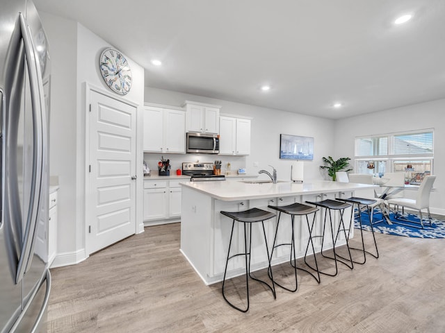 kitchen featuring a center island with sink, sink, light hardwood / wood-style floors, white cabinetry, and stainless steel appliances