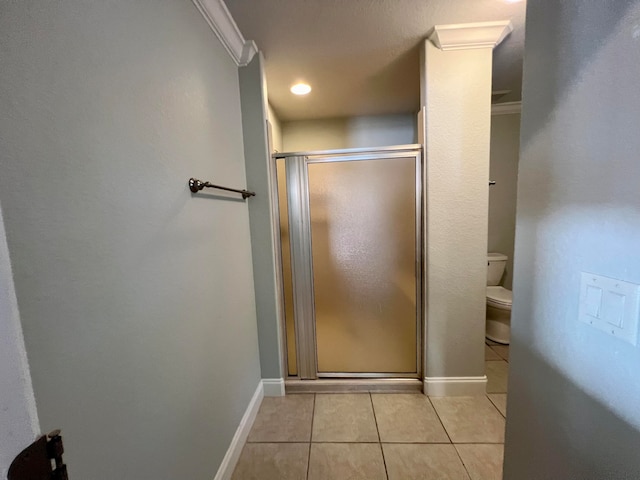 bathroom featuring tile patterned floors, toilet, a shower with door, and crown molding