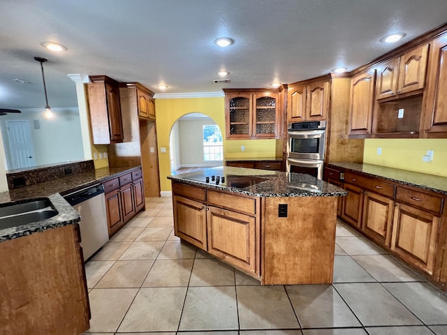 kitchen with hanging light fixtures, dark stone countertops, ornamental molding, light tile patterned flooring, and stainless steel appliances