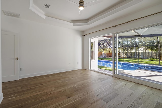 empty room with hardwood / wood-style flooring, ceiling fan, and a tray ceiling