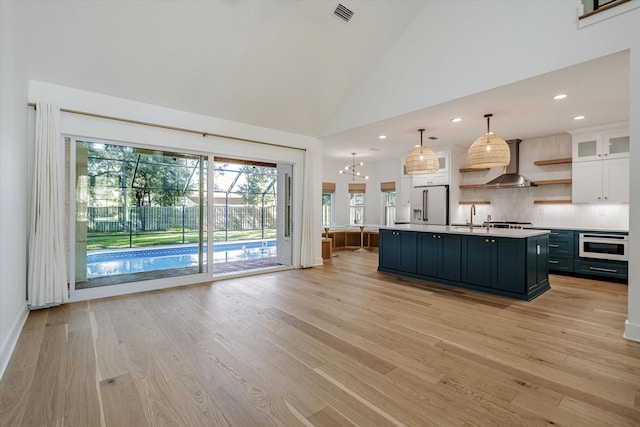 kitchen with white appliances, white cabinets, hanging light fixtures, an island with sink, and light hardwood / wood-style floors