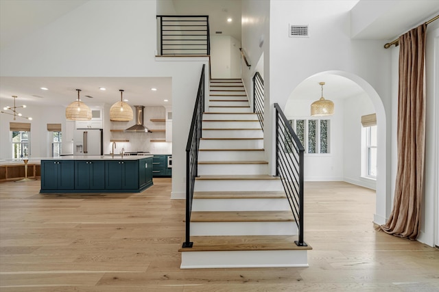 stairs with sink, a towering ceiling, wood-type flooring, and a notable chandelier