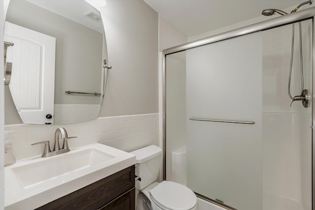 bathroom with vanity, toilet, a shower with door, and tile walls