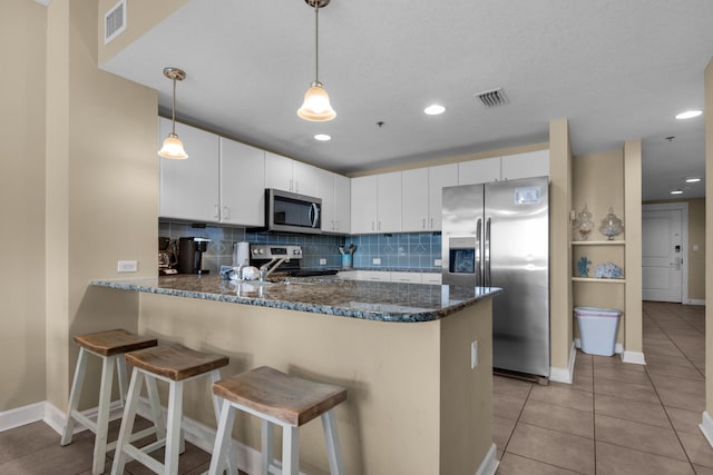 kitchen with white cabinetry, hanging light fixtures, stainless steel appliances, kitchen peninsula, and decorative backsplash