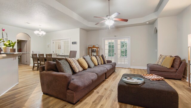 living room with ceiling fan with notable chandelier, light hardwood / wood-style floors, and a tray ceiling