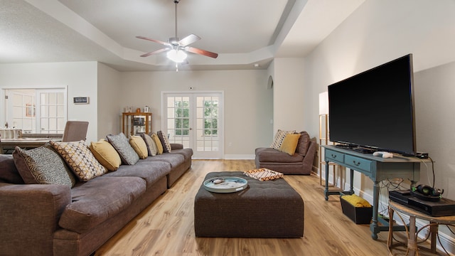 living room with a raised ceiling, ceiling fan, and light hardwood / wood-style flooring