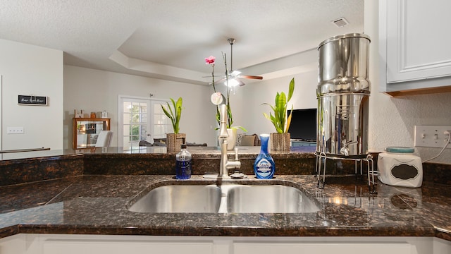 kitchen with white cabinets, ceiling fan, dark stone counters, and sink