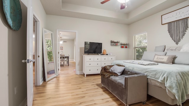 bedroom featuring a tray ceiling, multiple windows, ceiling fan, and light hardwood / wood-style floors