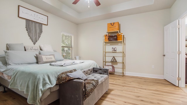 bedroom with a raised ceiling, ceiling fan, and light hardwood / wood-style floors