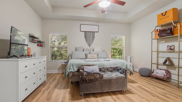 bedroom with a tray ceiling, multiple windows, ceiling fan, and light hardwood / wood-style flooring