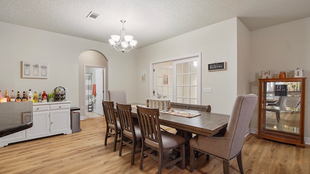 dining area with a textured ceiling, an inviting chandelier, and light hardwood / wood-style flooring