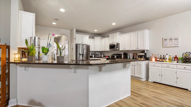 kitchen with kitchen peninsula, a breakfast bar, stainless steel appliances, light hardwood / wood-style flooring, and white cabinetry