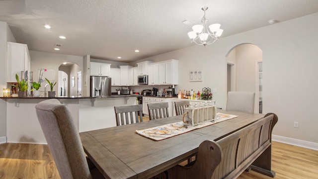 dining space featuring a textured ceiling, light hardwood / wood-style floors, and an inviting chandelier