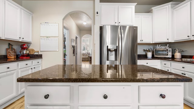 kitchen with dark stone counters, stainless steel fridge with ice dispenser, a center island, light hardwood / wood-style floors, and white cabinetry