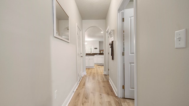 hall with light wood-type flooring and a textured ceiling