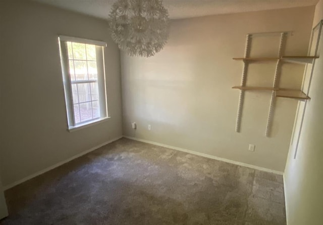 spare room with a notable chandelier and dark colored carpet