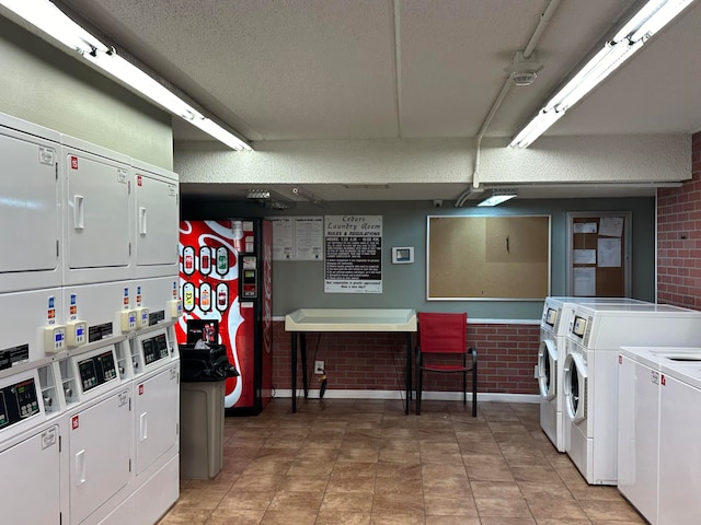 laundry room featuring washer and clothes dryer, stacked washing maching and dryer, a textured ceiling, and brick wall