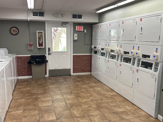 clothes washing area with washer and clothes dryer, brick wall, and stacked washer and clothes dryer