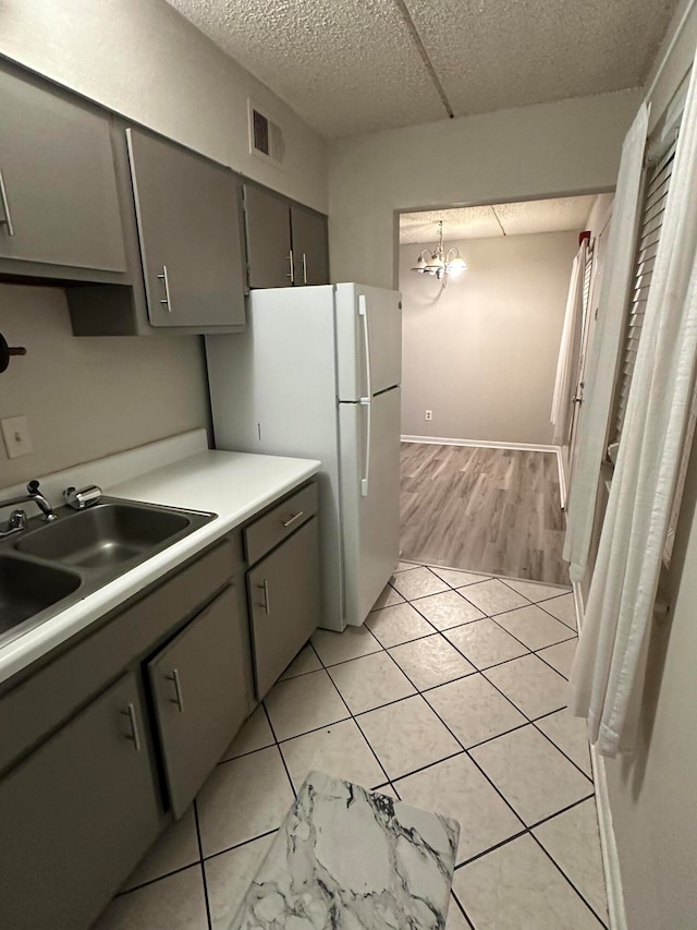 kitchen featuring gray cabinetry, an inviting chandelier, white refrigerator, sink, and light wood-type flooring