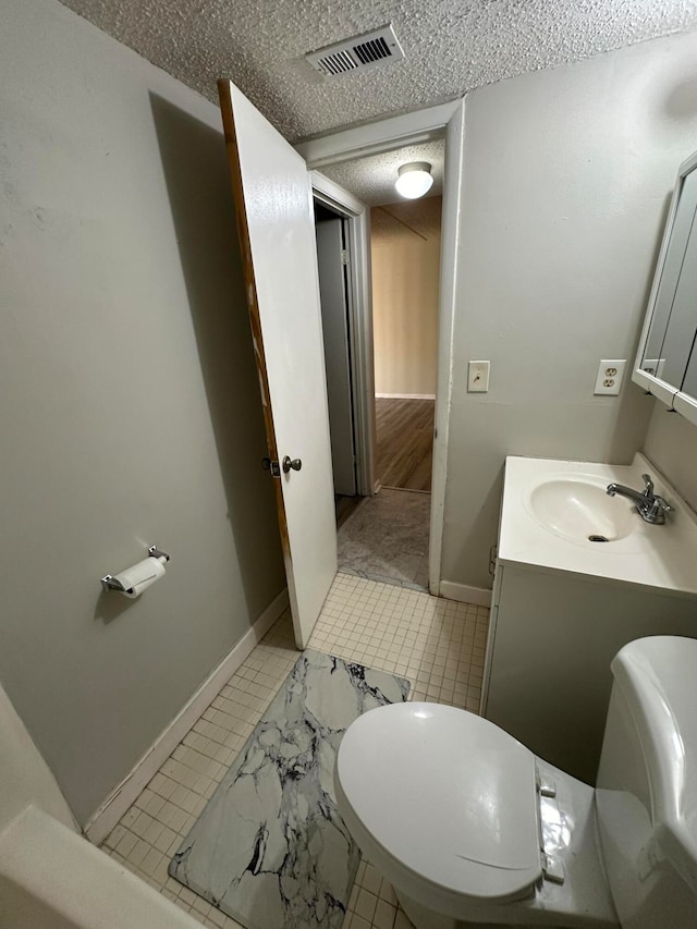 bathroom with toilet, a textured ceiling, vanity, and tile patterned floors