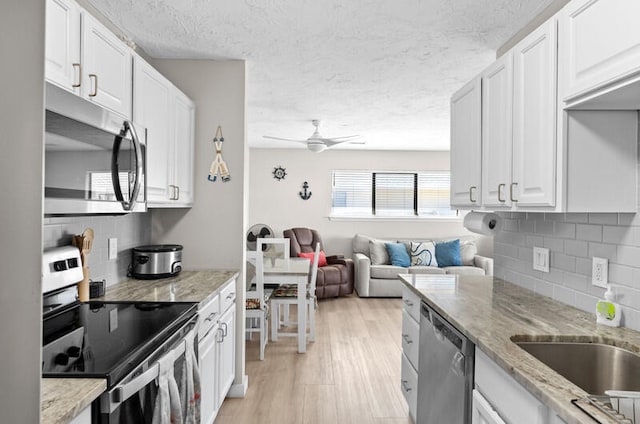 kitchen featuring white cabinets, light stone counters, appliances with stainless steel finishes, and light hardwood / wood-style flooring