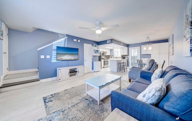 living room with light wood-type flooring and ceiling fan with notable chandelier