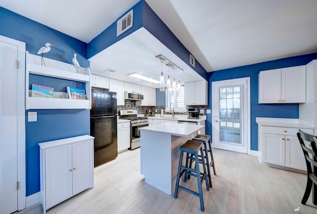 kitchen with appliances with stainless steel finishes, a kitchen island, white cabinetry, and pendant lighting