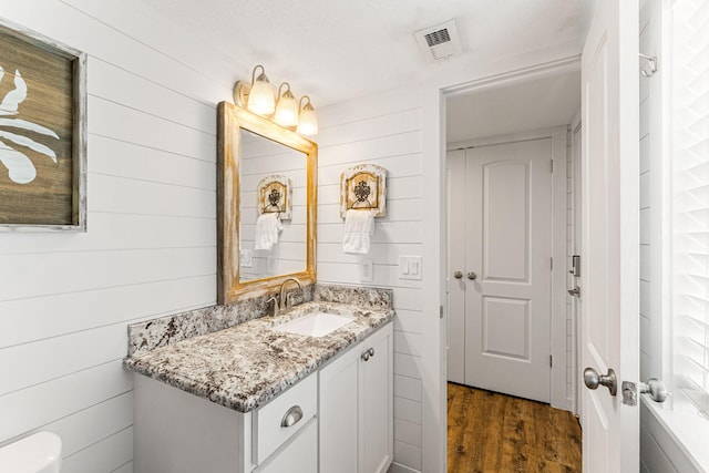 bathroom featuring vanity, wood-type flooring, a textured ceiling, and wooden walls