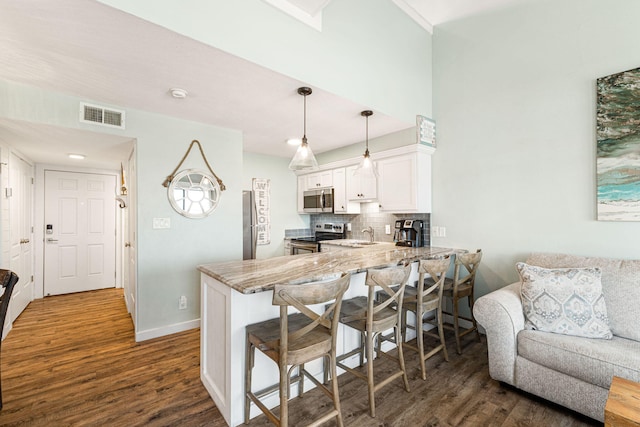 kitchen with white cabinetry, dark wood-type flooring, a kitchen breakfast bar, kitchen peninsula, and appliances with stainless steel finishes