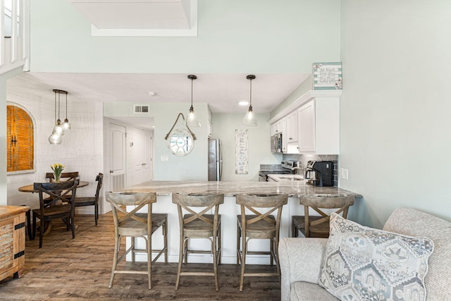 kitchen with a kitchen bar, appliances with stainless steel finishes, white cabinetry, and dark wood-type flooring