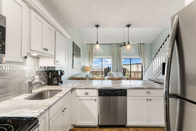 kitchen featuring sink, appliances with stainless steel finishes, white cabinetry, light stone counters, and kitchen peninsula