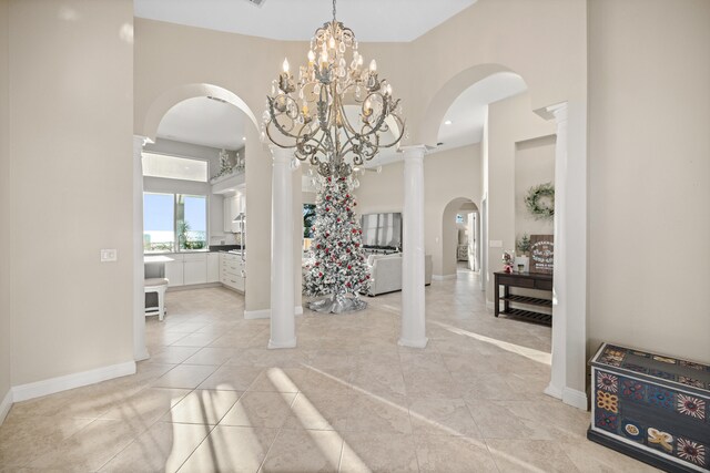 foyer entrance featuring decorative columns, light tile patterned floors, and a chandelier